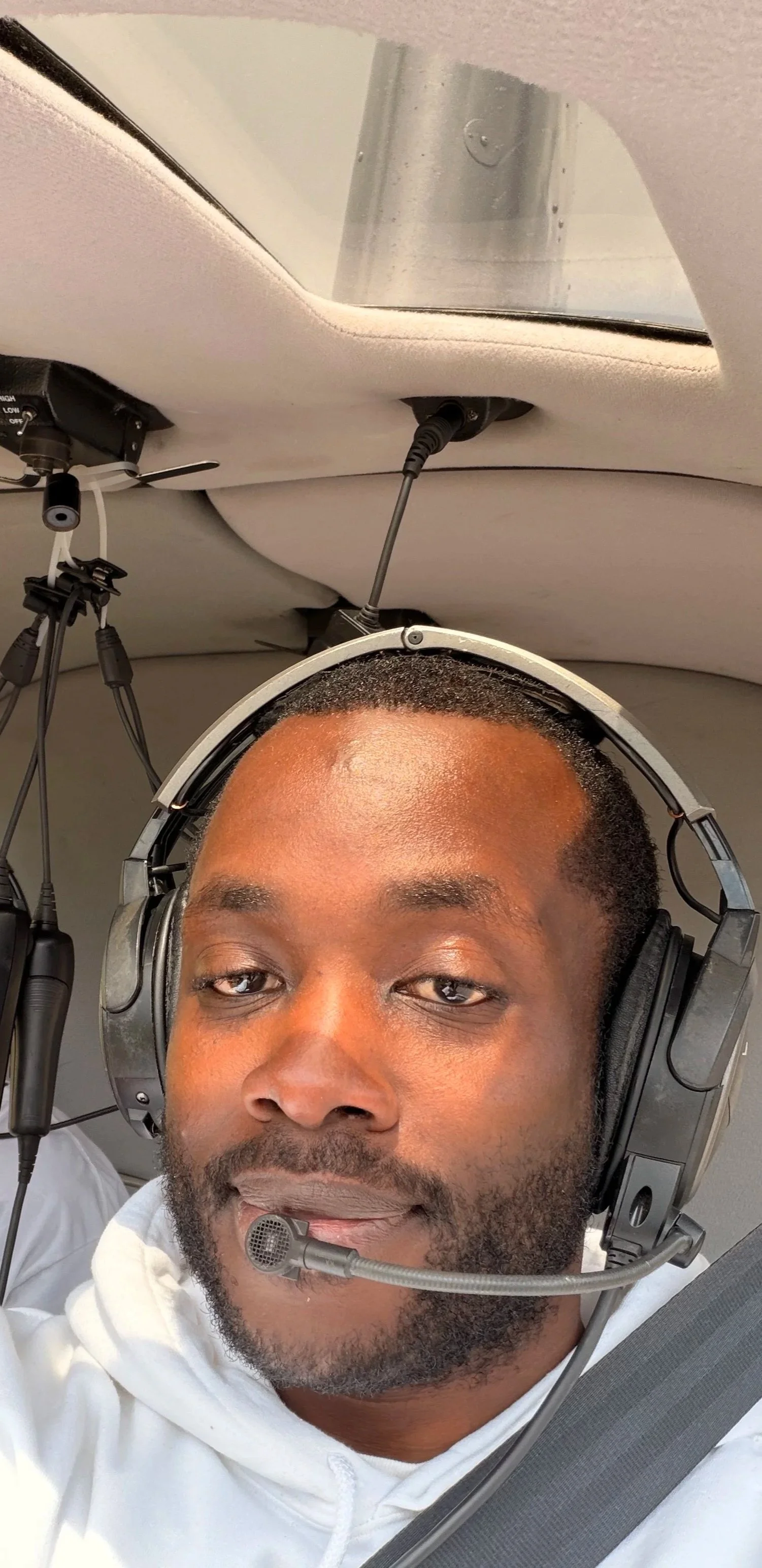 A man wearing a pilot headset takes a selfie inside an aircraft.