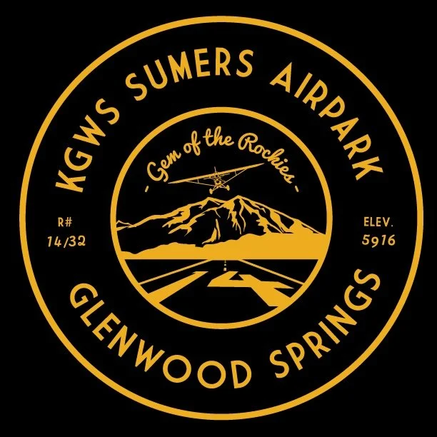 A circular logo with yellow text and graphics on a black background. It reads "HGWS Sumers Airpark" and "Glenwood Springs" around the edge. The center features a mountain with a runway and a small airplane flying above, along with the text "Gem of the Rockies." Additional details include "R# 14/32" and "ELEV. 5916."
