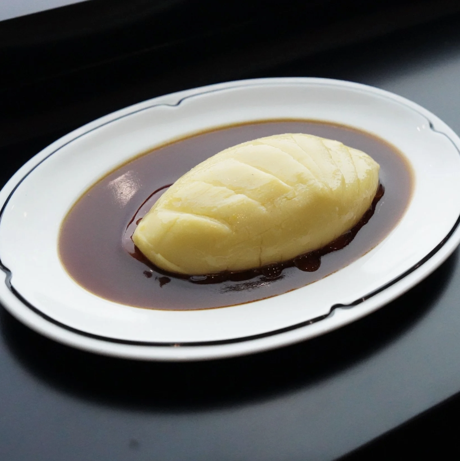 A white oval plate with a scoop of yellow ice cream served in a pool of chocolate sauce.