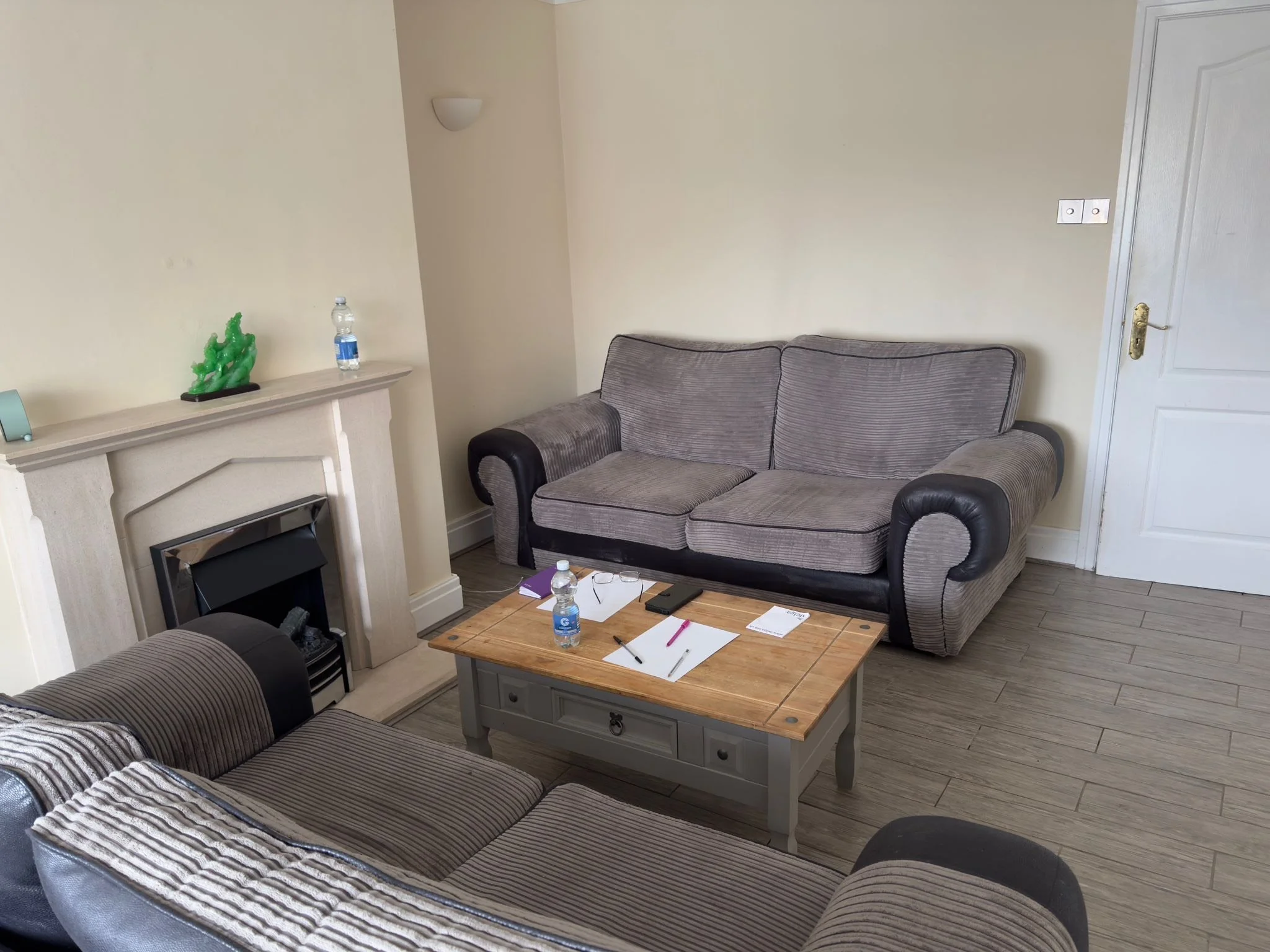Living room with gray sofas, a wooden coffee table, a fireplace, and a shelf with decorative items and a water bottle.
