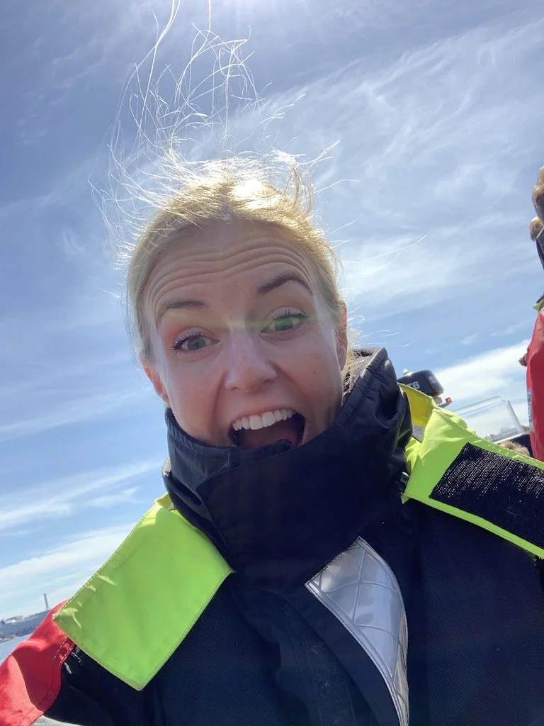 Glad kvinna med solklart leende, utomhus mot klar blå himmel, i livräddningsutrustning.