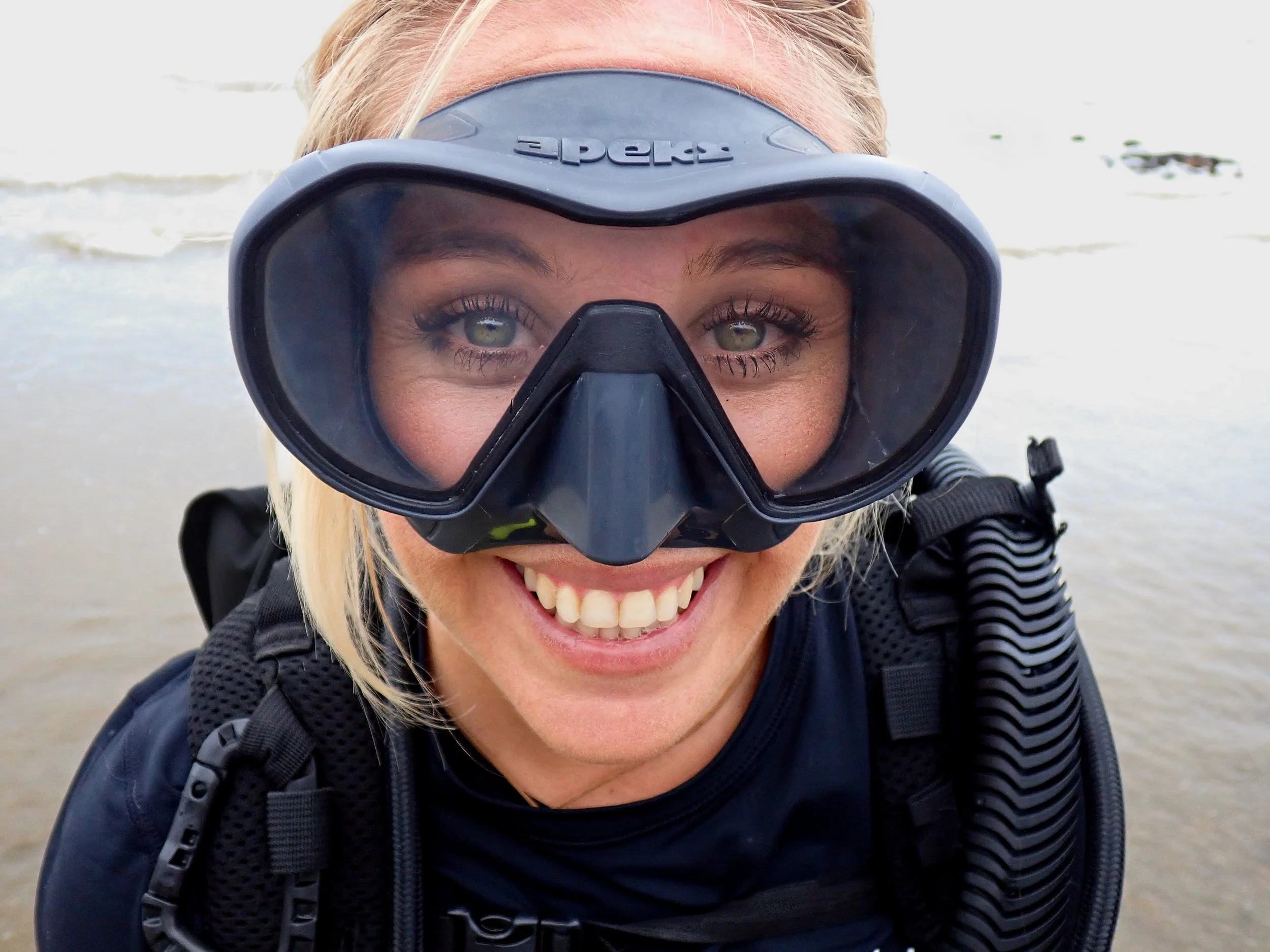 A smiling woman at the beach wearing snorkeling gear, including a mask and a wetsuit. Alyssa Mitchell.
