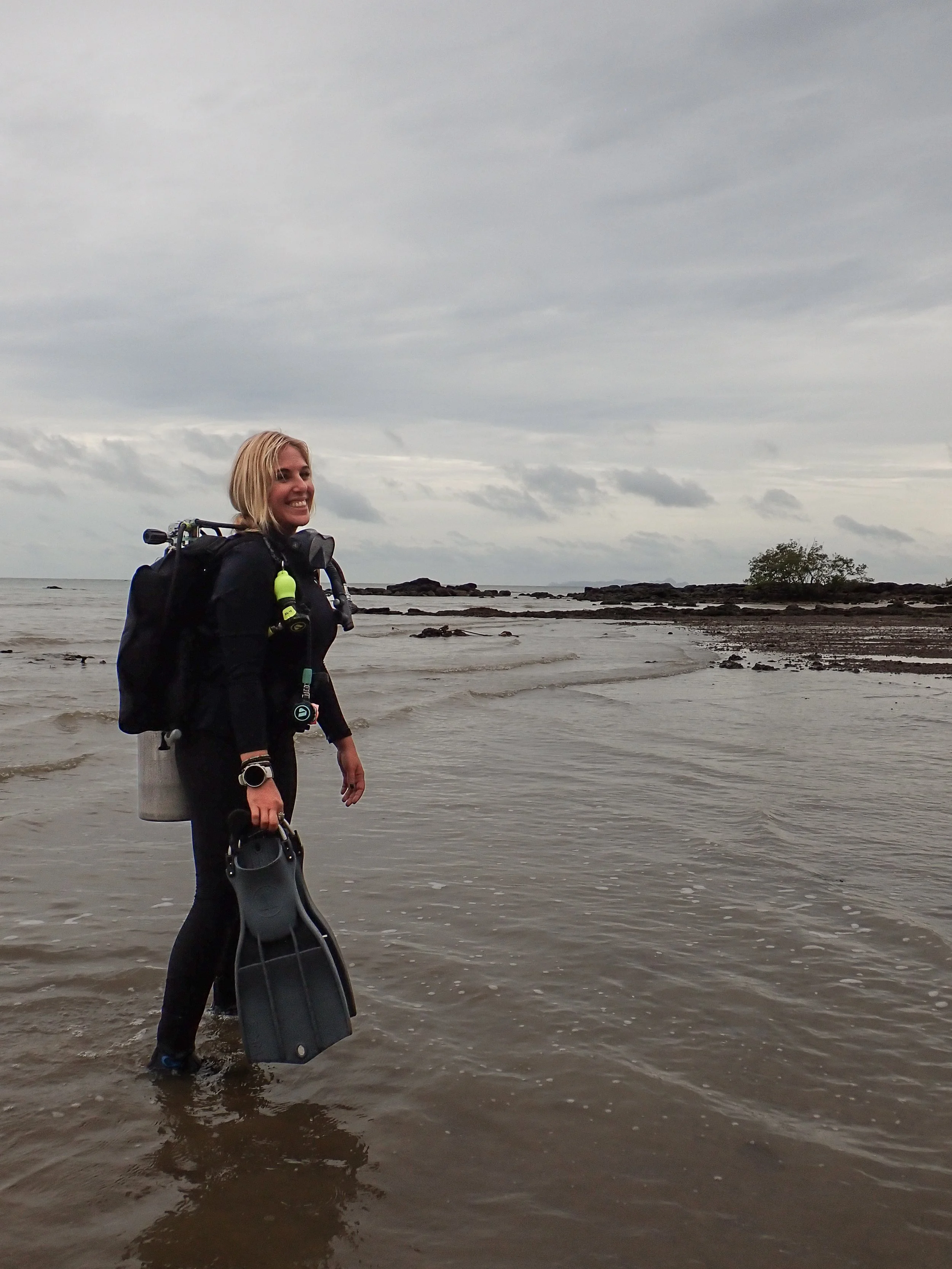 Women scuba diver going for a dive on a beach, smiling.