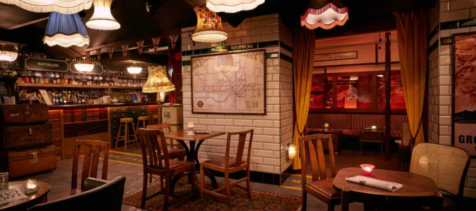 Cozy pub or restaurant interior with dim warm lighting, wooden tables and chairs, vintage lamps, a bar with liquor bottles, and yellow curtains.