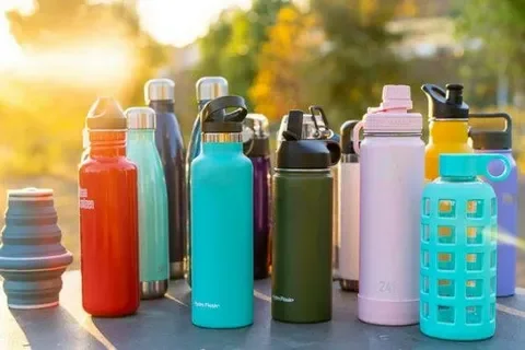 A variety of colorful reusable water bottles arranged outdoors on a sunny day.