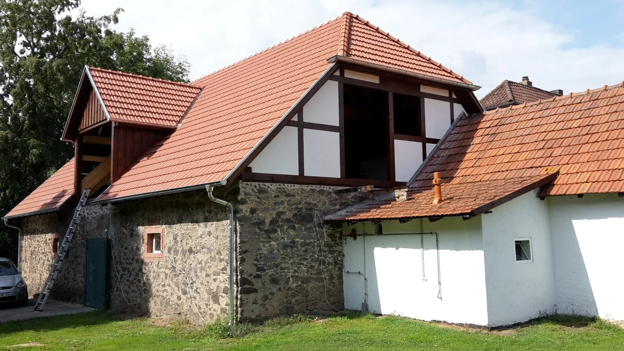 Ein haus mit roten Ziegeldächern und einem gemauerten unteren Teil, teilweise renoviert, mit einer Leiter am linken Rand.