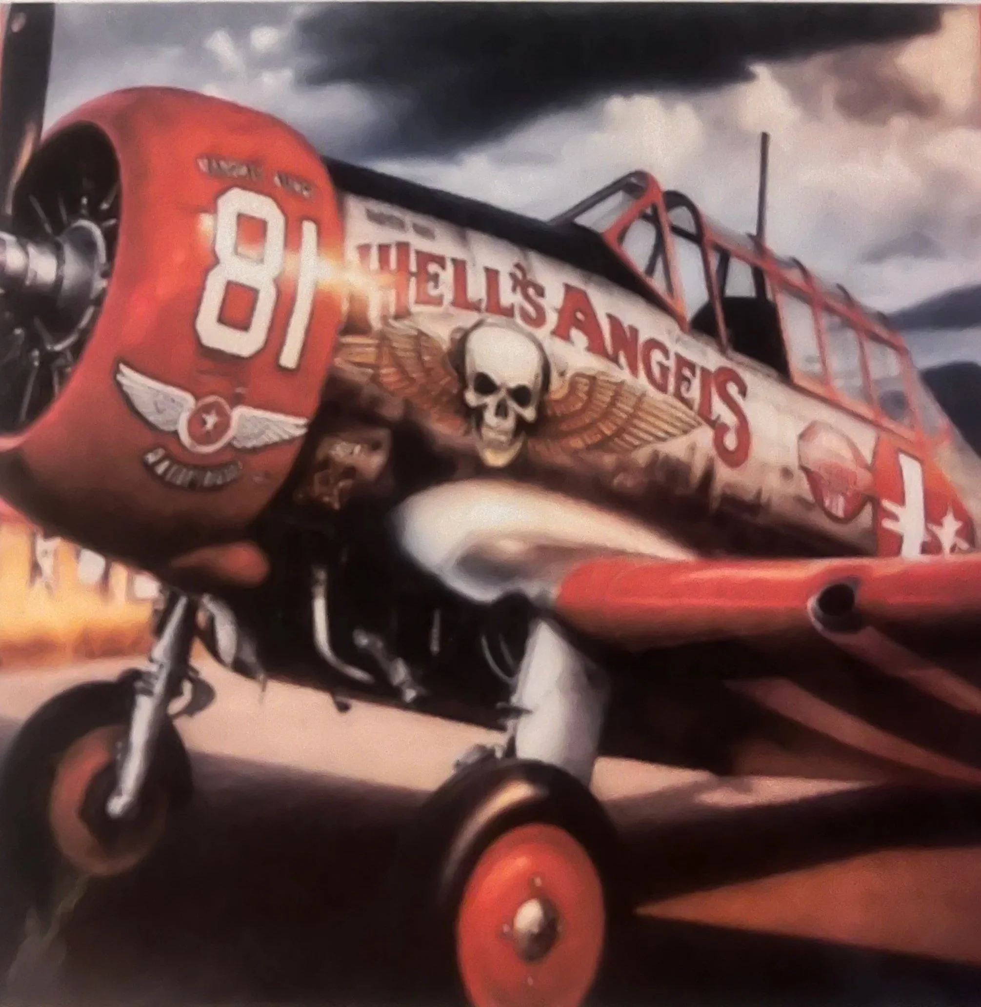 Un avión antiguo con un dibujo en el morro de color rojo que muestra una calavera con alas, el texto "Hell's Angels" y el número 81, sobre un cielo nublado.