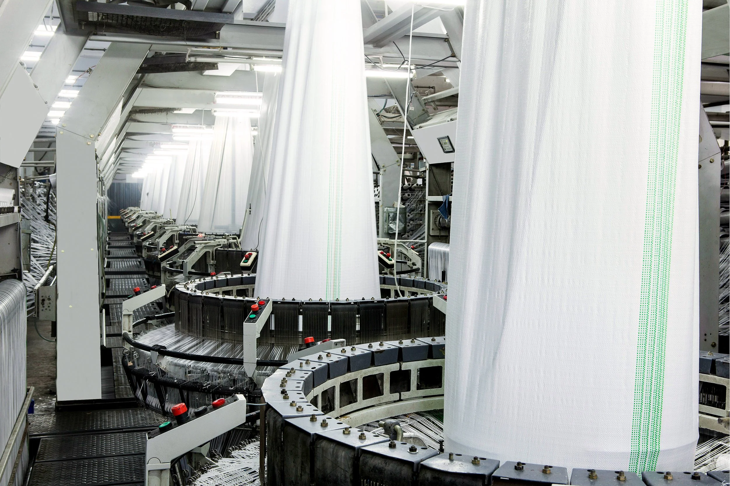 Industrial textile manufacturing machine with large spools of white fabric on a circular weaving or knitting machine.