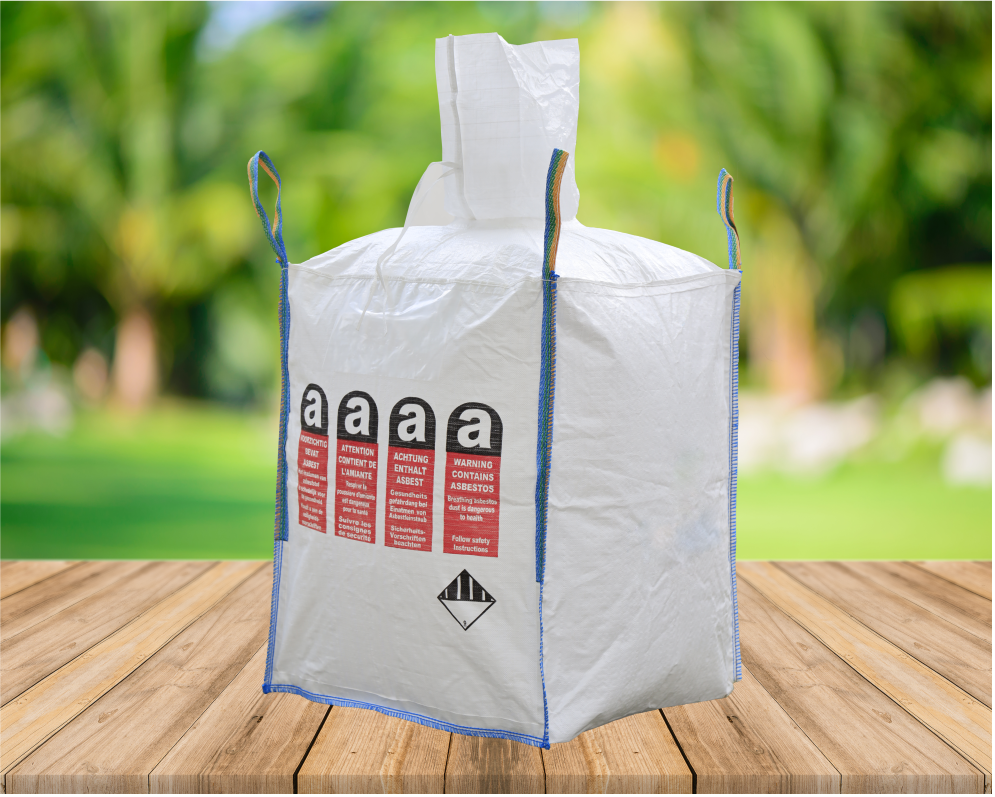 A white industrial bag with hazardous material warning labels, placed on a wooden surface with a blurred green outdoor background.