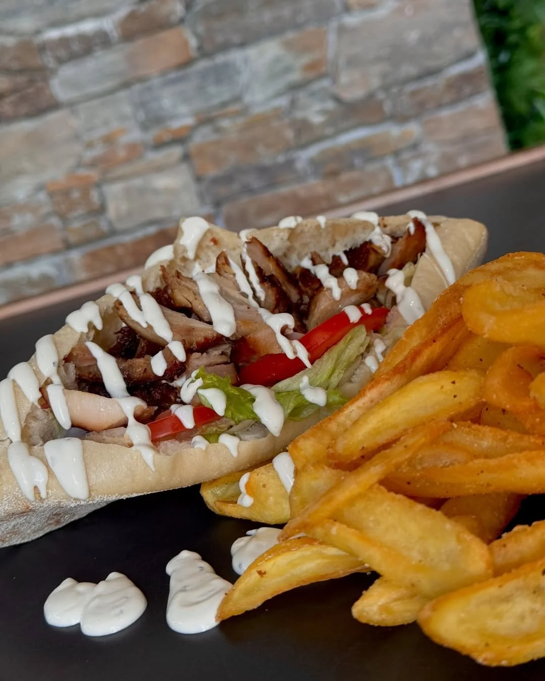 Sandwich pita garni de poulet, légumes et sauce, accompagné de frites maison, sur une assiette noire.