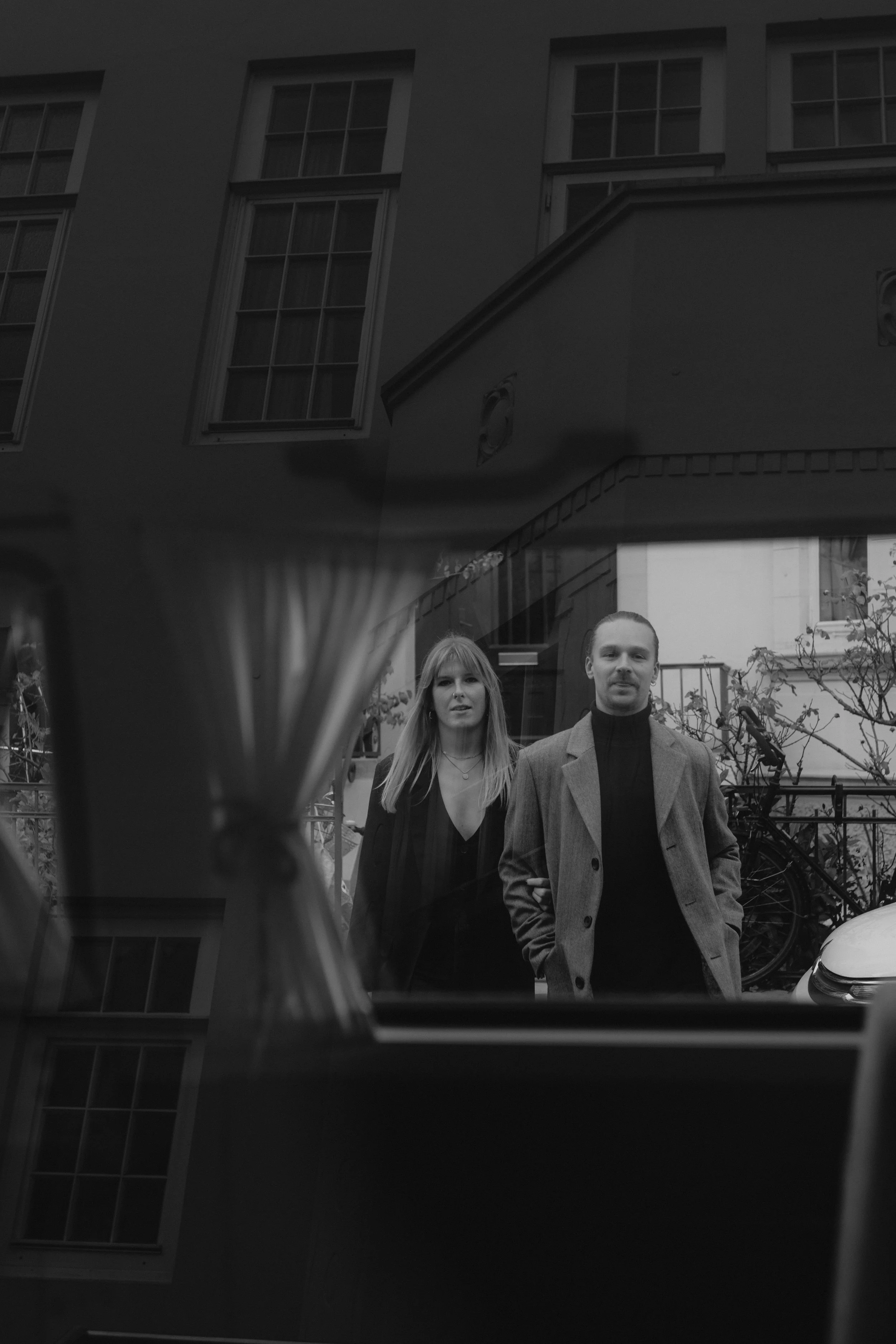 Zwei Menschen, ein Mann und eine Frau, stehen draußen vor einem Fenster und schauen hinein, während die Aufnahme von innen gemacht wurde.