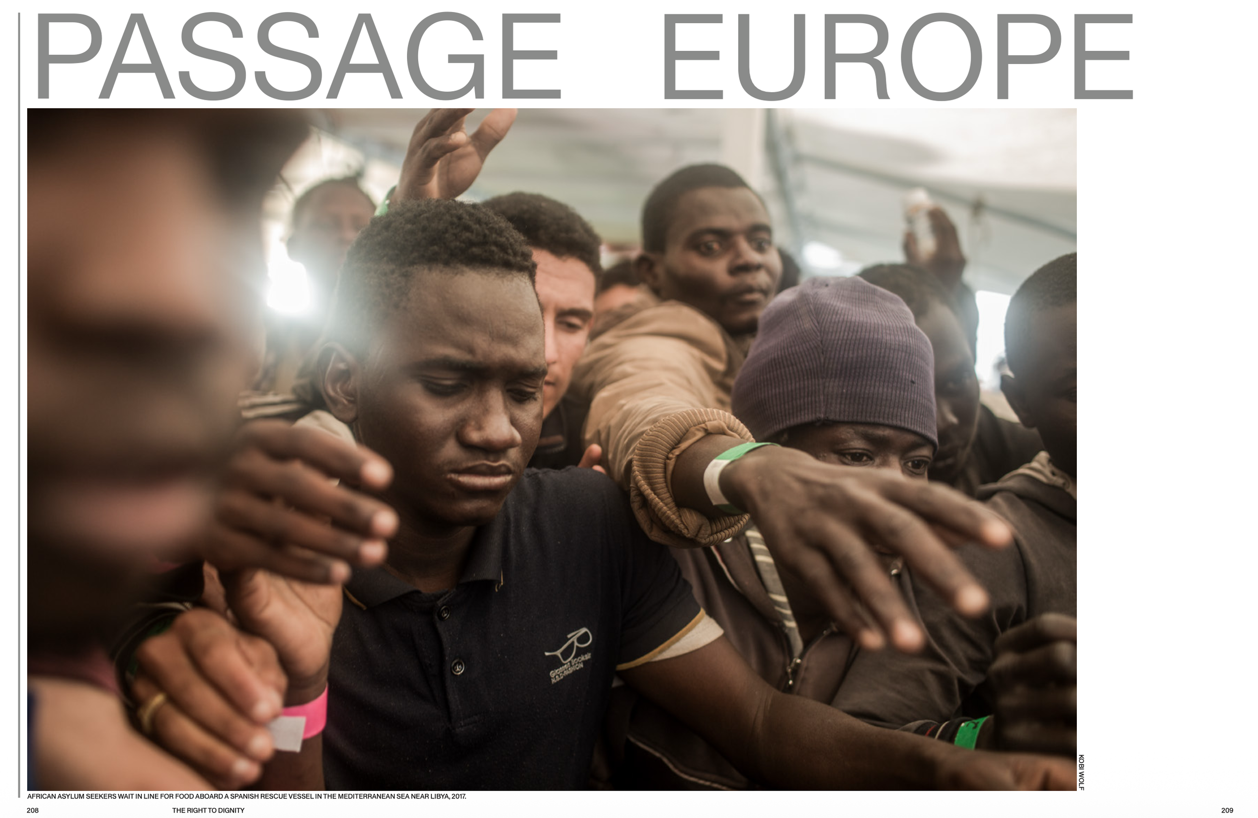 Group of African asylum seekers standing in a line with arms crossed over their chests, waiting for food aboard a Spanish rescue vessel in the Mediterranean Sea near Libya, 2017.