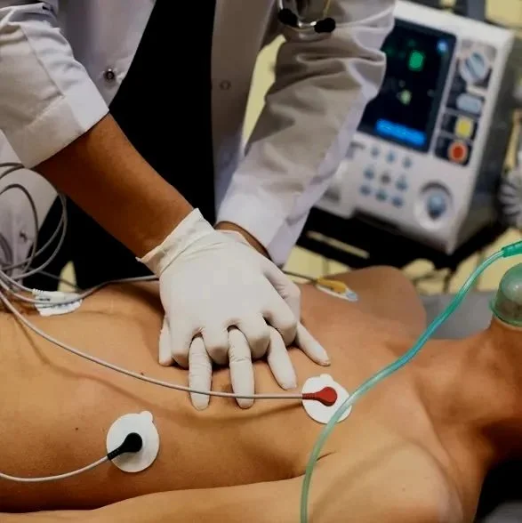 Medical professional performing an ECG or monitoring heart activity on a patient’s bare chest in a hospital setting.