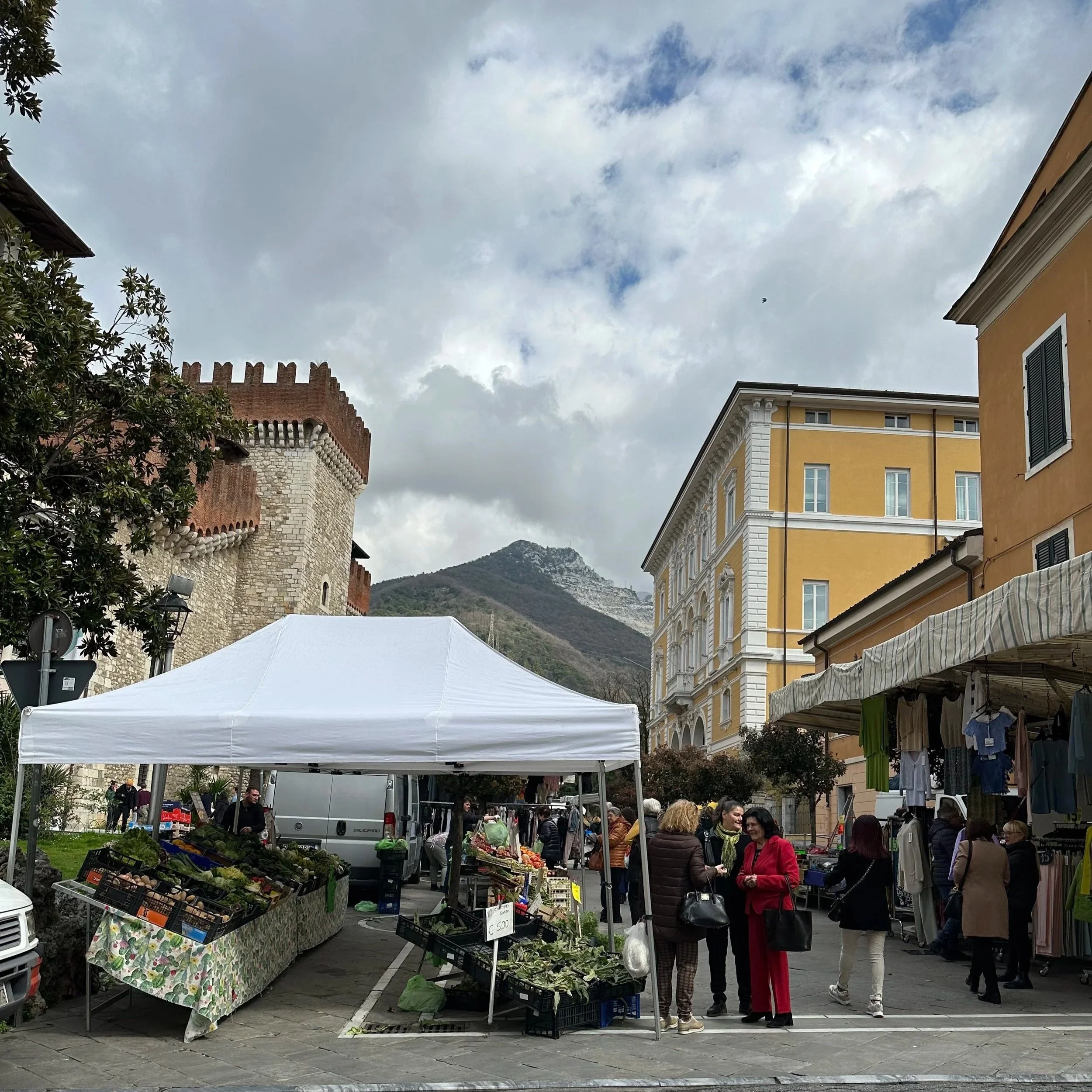 Open-air farmers’ market in Carrara, Tuscany, Italy with locals shopping for fresh meats, cheeses, clothing and artisan goods Italy