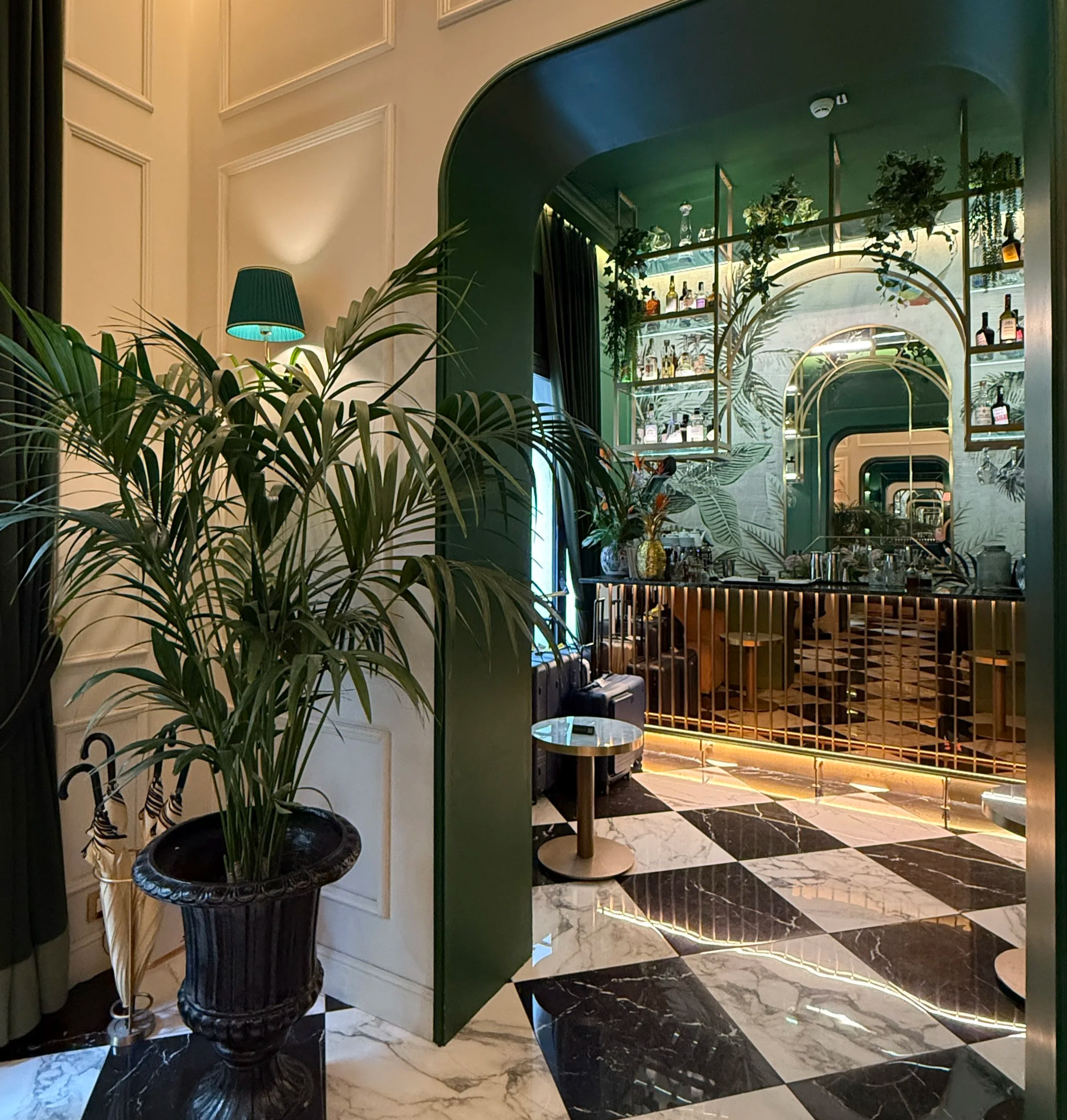 Reception area at the Green Gold Bar in La Gemma Hotel, Florence, featuring emerald-toned interiors, polished brass accents, lush potted plants, and a refined front desk framed by warm, ambient lighting, alcohol, Italian wine