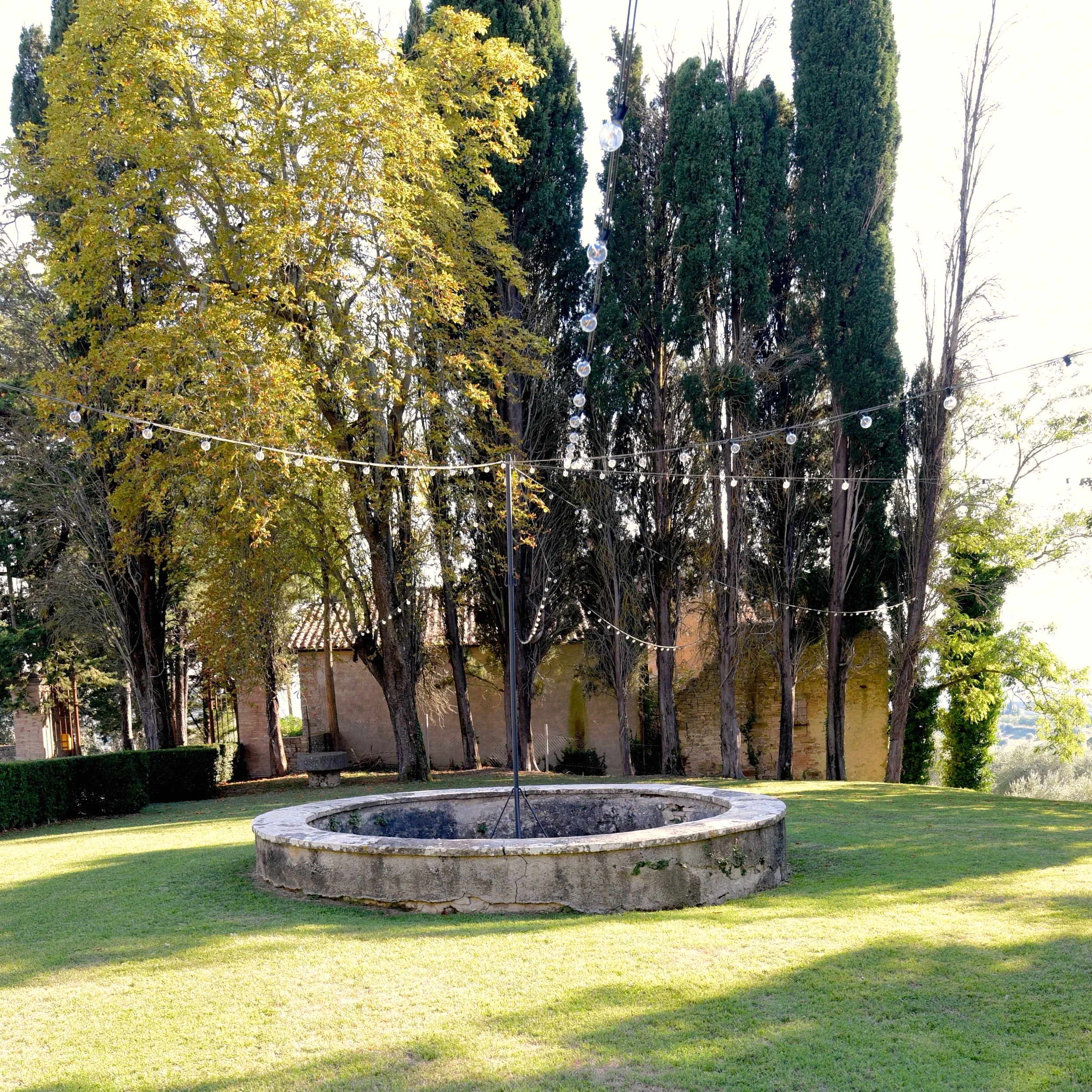 Traditional stone well on a green lawn in the Umbrian countryside.