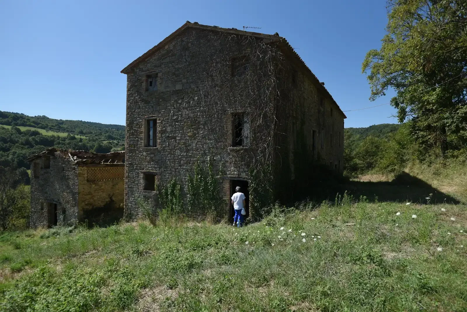 Stone farmhouse in the Umbrian countryside, with Elvira entering the doorway.