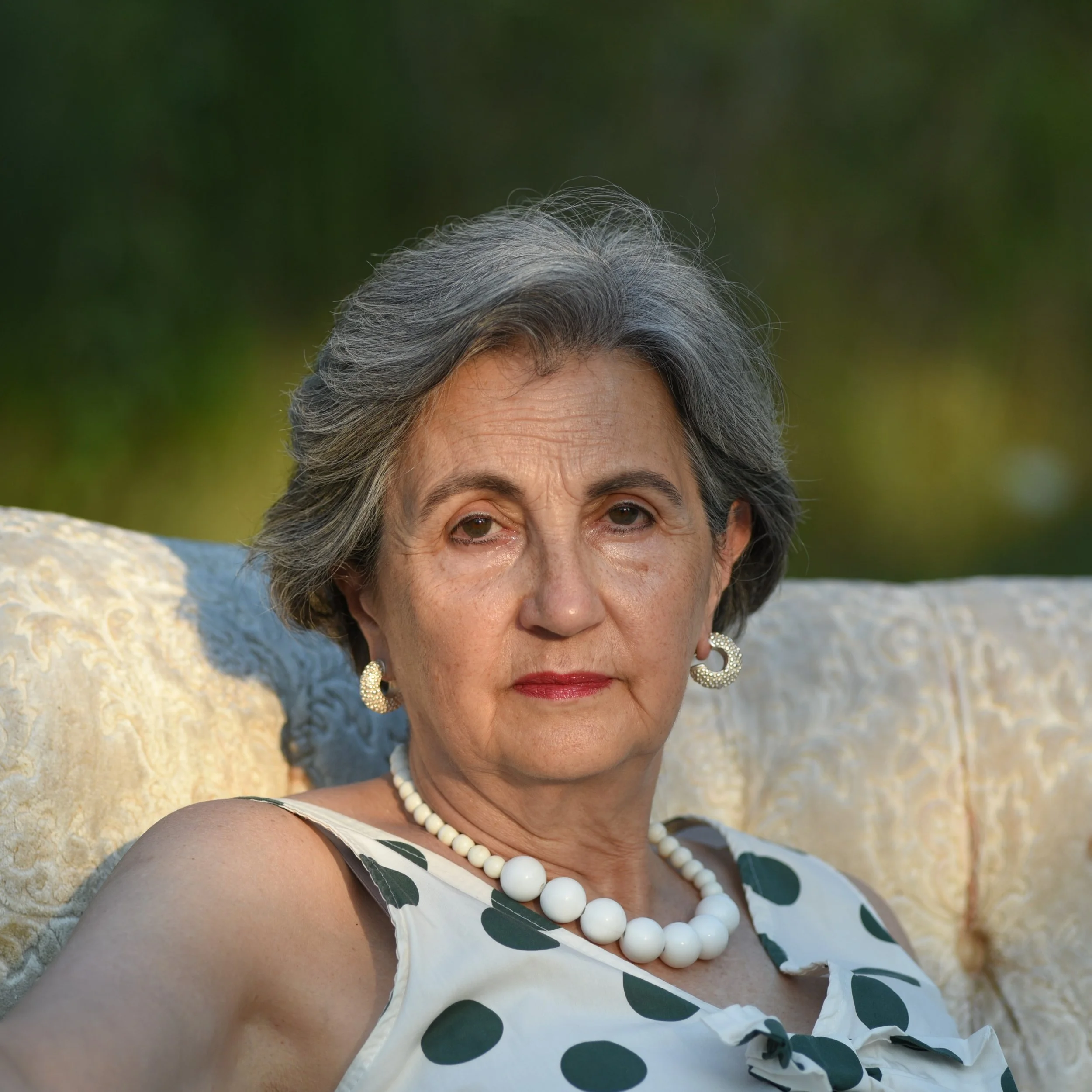 Elegant portrait of Elvira Lato in pearls and white dress, outdoors in Umbria.