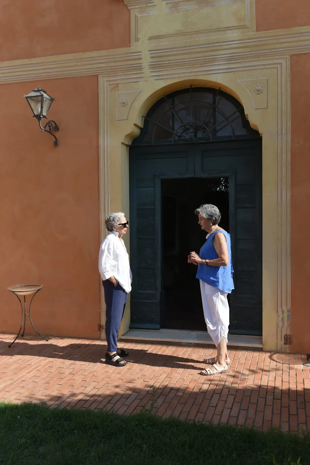 Two women conversing at the entrance of a traditional Umbrian orange home.