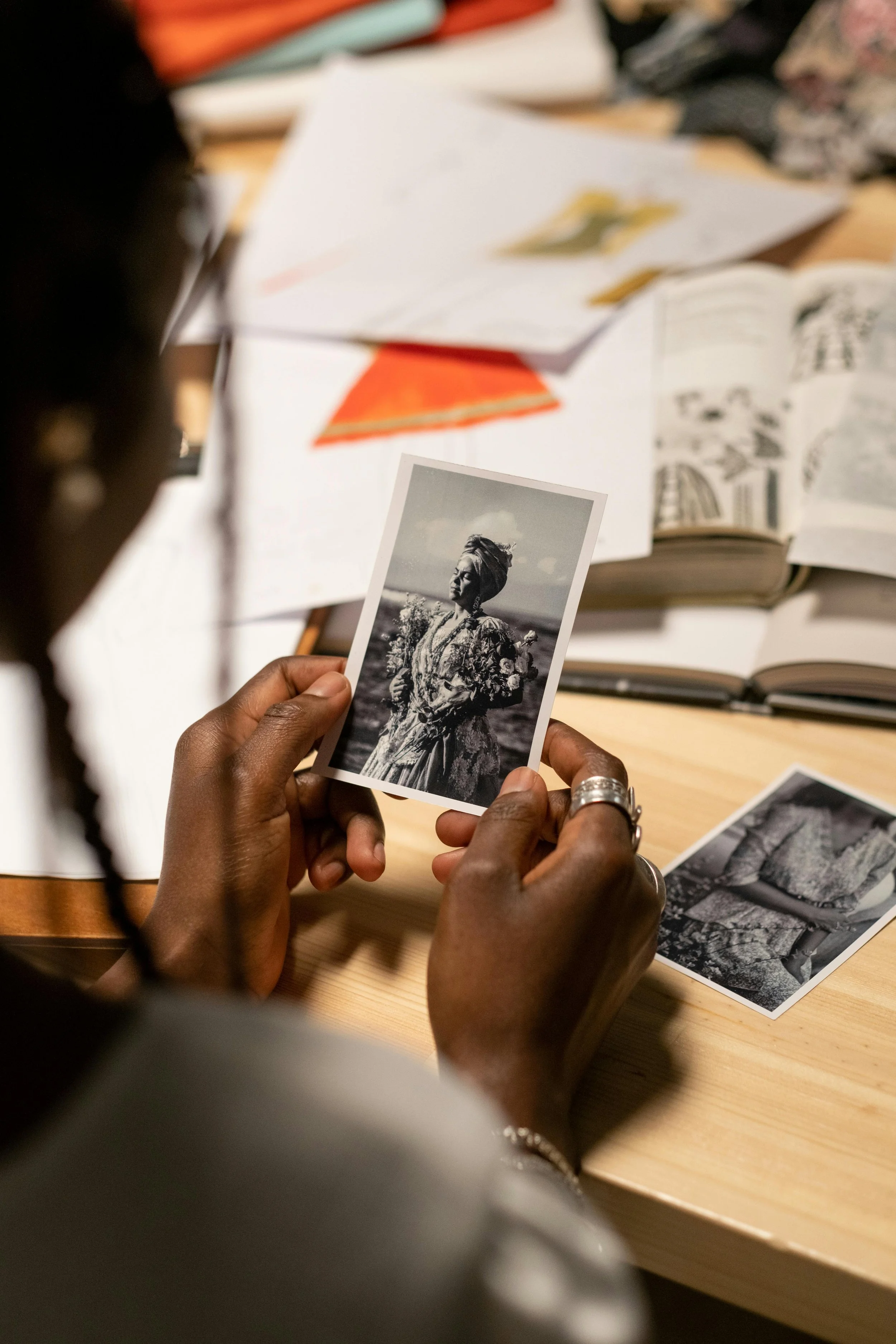 Persoon houdt een zwart-wit foto van een vrouw met bloemen, omringd door boeken en documenten op een tafel.
