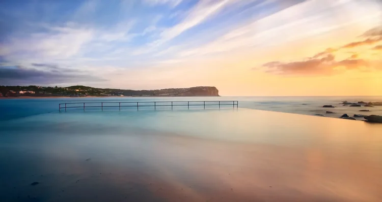 Macmasters Beach ocean pool at sunrise with calm waves and distant headland, Central Coast NSW