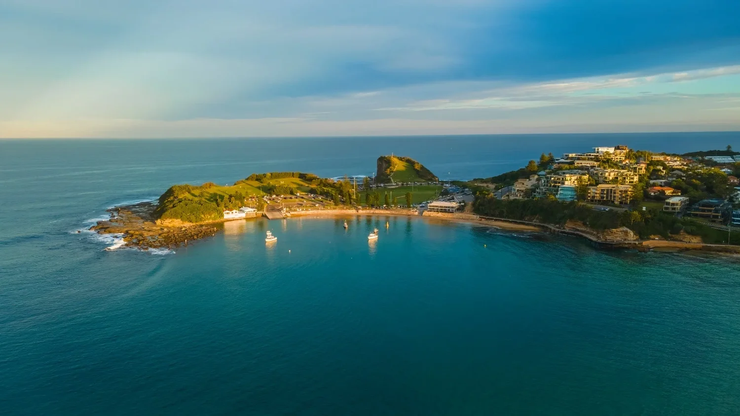 Aerial view of Terrigal headland with boats anchored in calm turquoise water at golden hour, Central Coast NSW