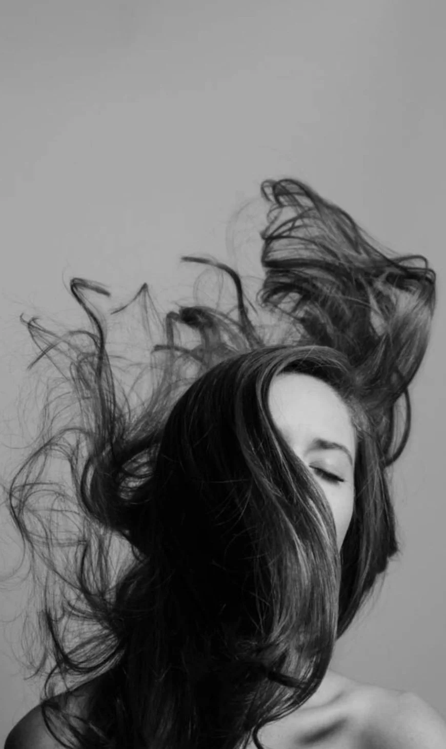 Black and white photo of a woman with long hair swept up, her face partially visible with closed eyes, against a plain background.