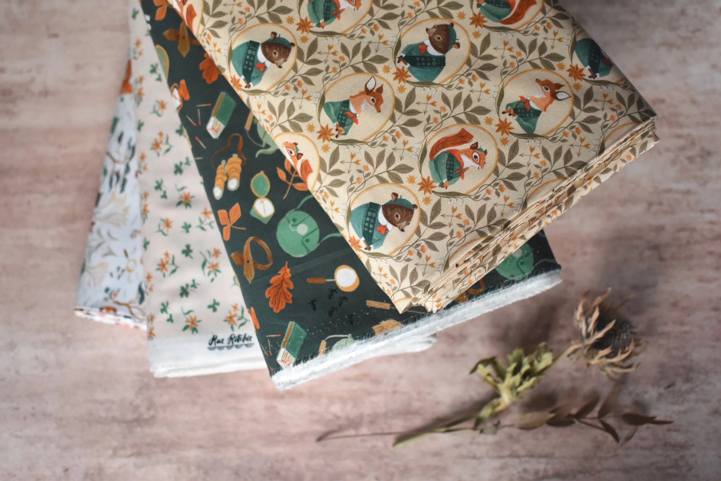 Stack of decorated paper napkins with woodland animal illustrations on a wooden surface, accompanied by dried plants.