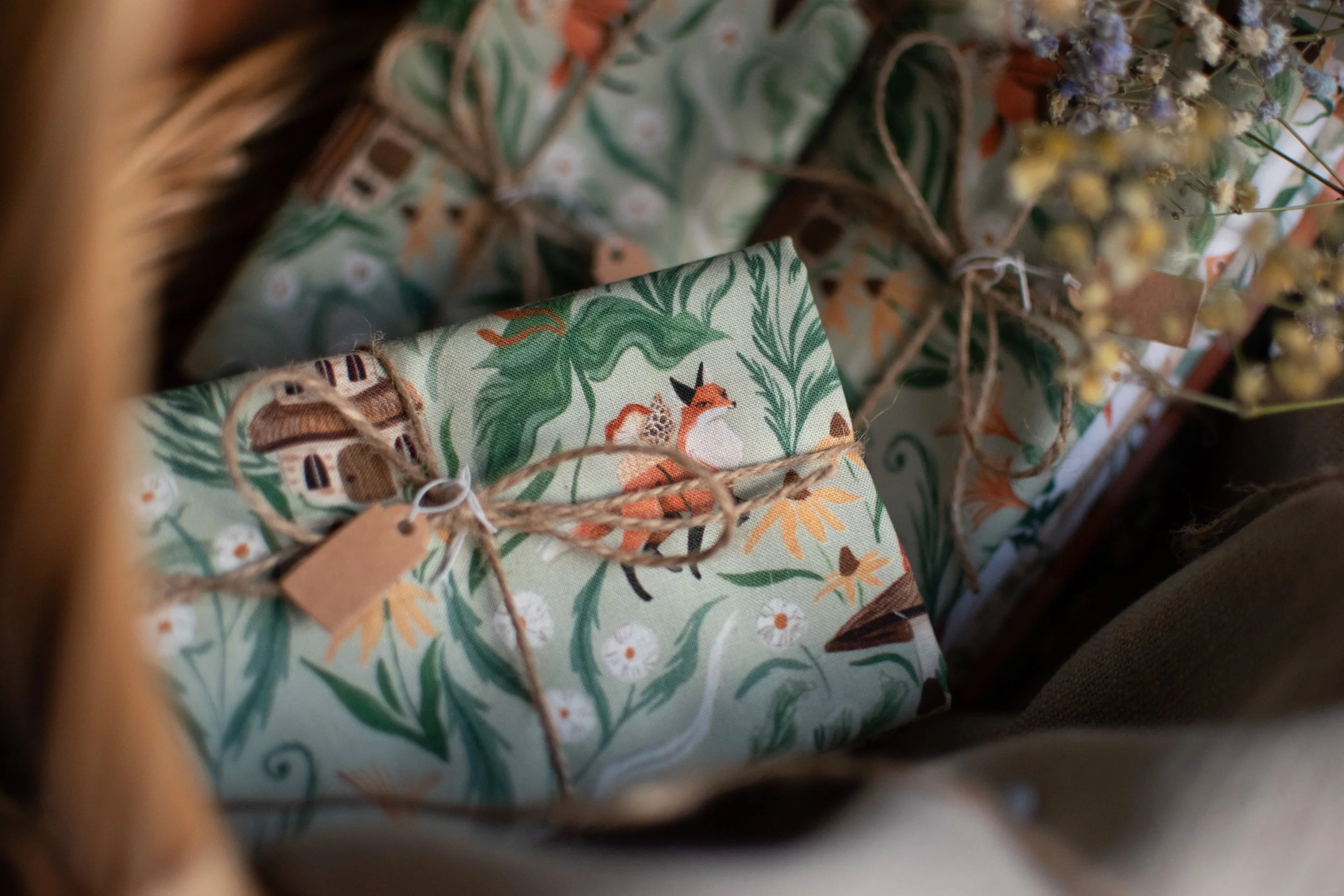 Wrapped presents with nature-themed, colorful paper, tied with twine and small tags, surrounded by dried flowers.