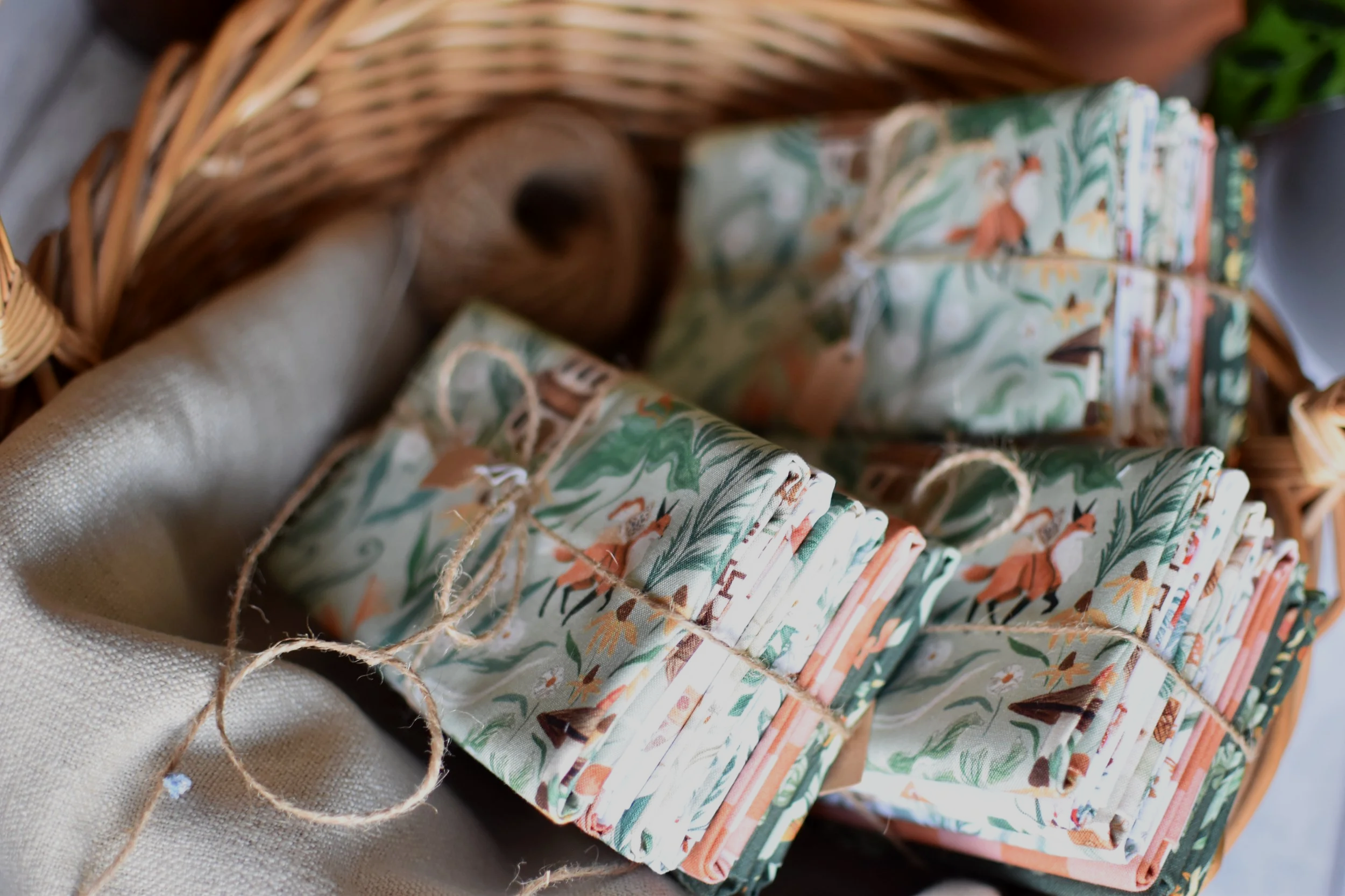 Bundles of fabric with colorful animal and plant designs, tied with string, in a wicker basket.