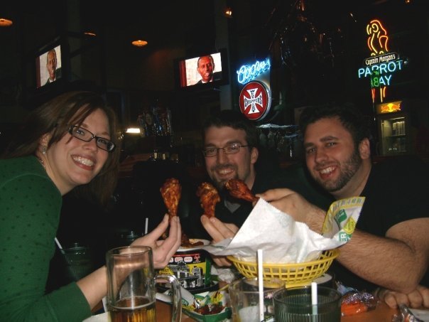Vox Rewatch hosts enjoying food together—three friends at a restaurant table raising chicken wings in a toast.
