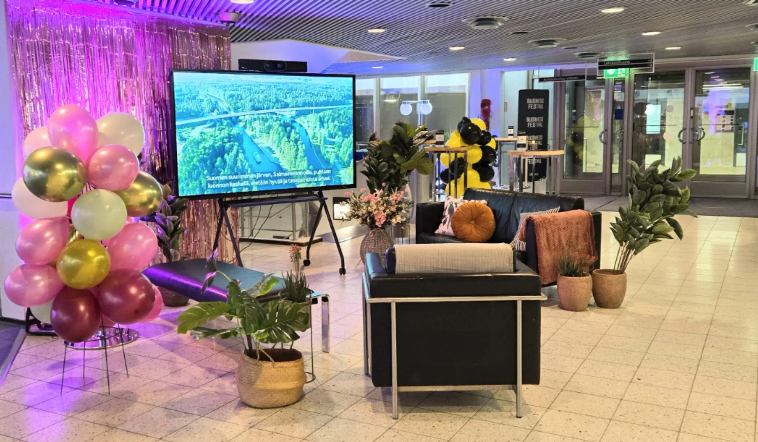 Modernin lounge-alueen sisustus, jossa on tummia sohvia, potted kasveja, suuri televisio ja lilat ja keltaiset ilmapallot yhdessä tapahtumatilassa.