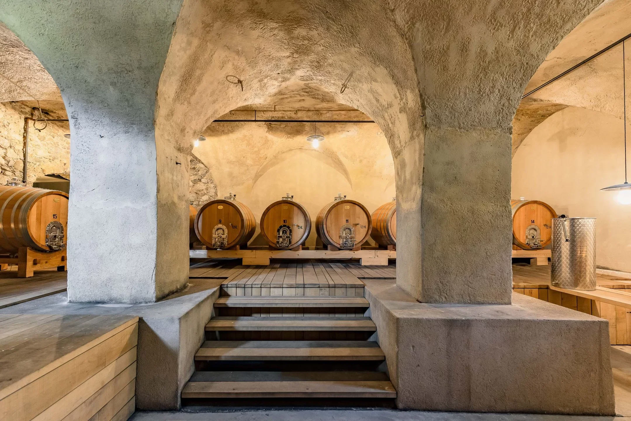A wine cellar with large wooden barrels, stone walls, and arched ceiling