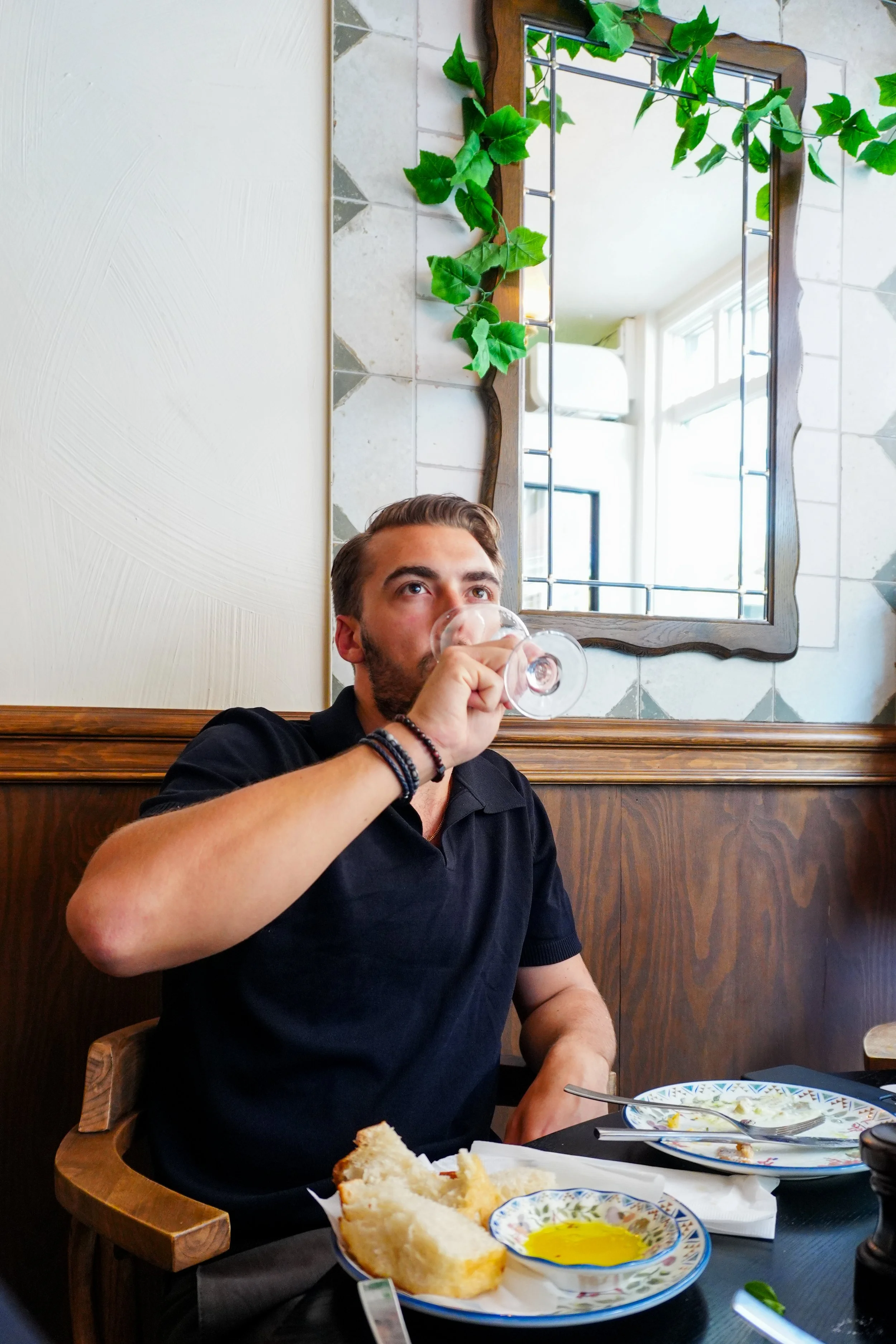 A young man in a tuxedo with a white bow tie smiling at a celebration, holding glasses of rosé wine.
