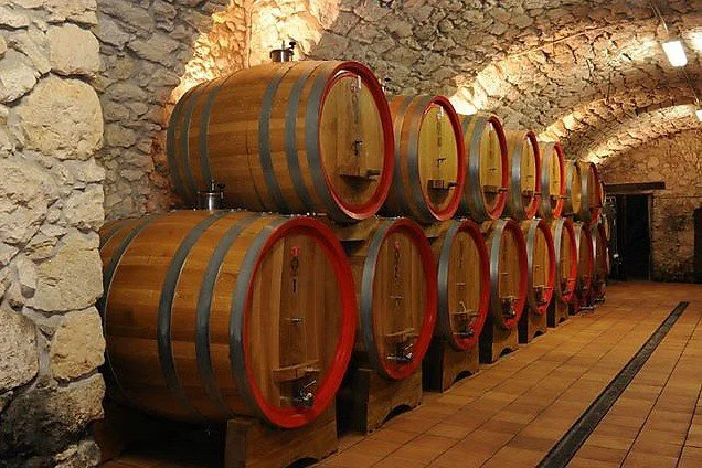 Rows of wooden wine barrels stored in a stone-walled cellar.