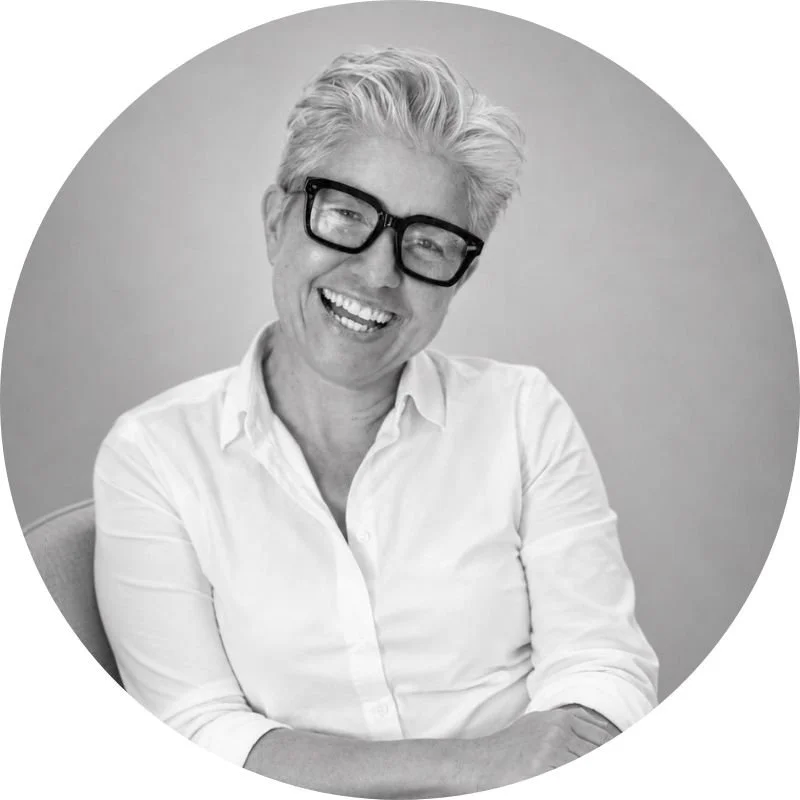 A smiling Dr Tanya Petersen with short, gray hair wearing black glasses and a white button-up shirt inside a circular frame.