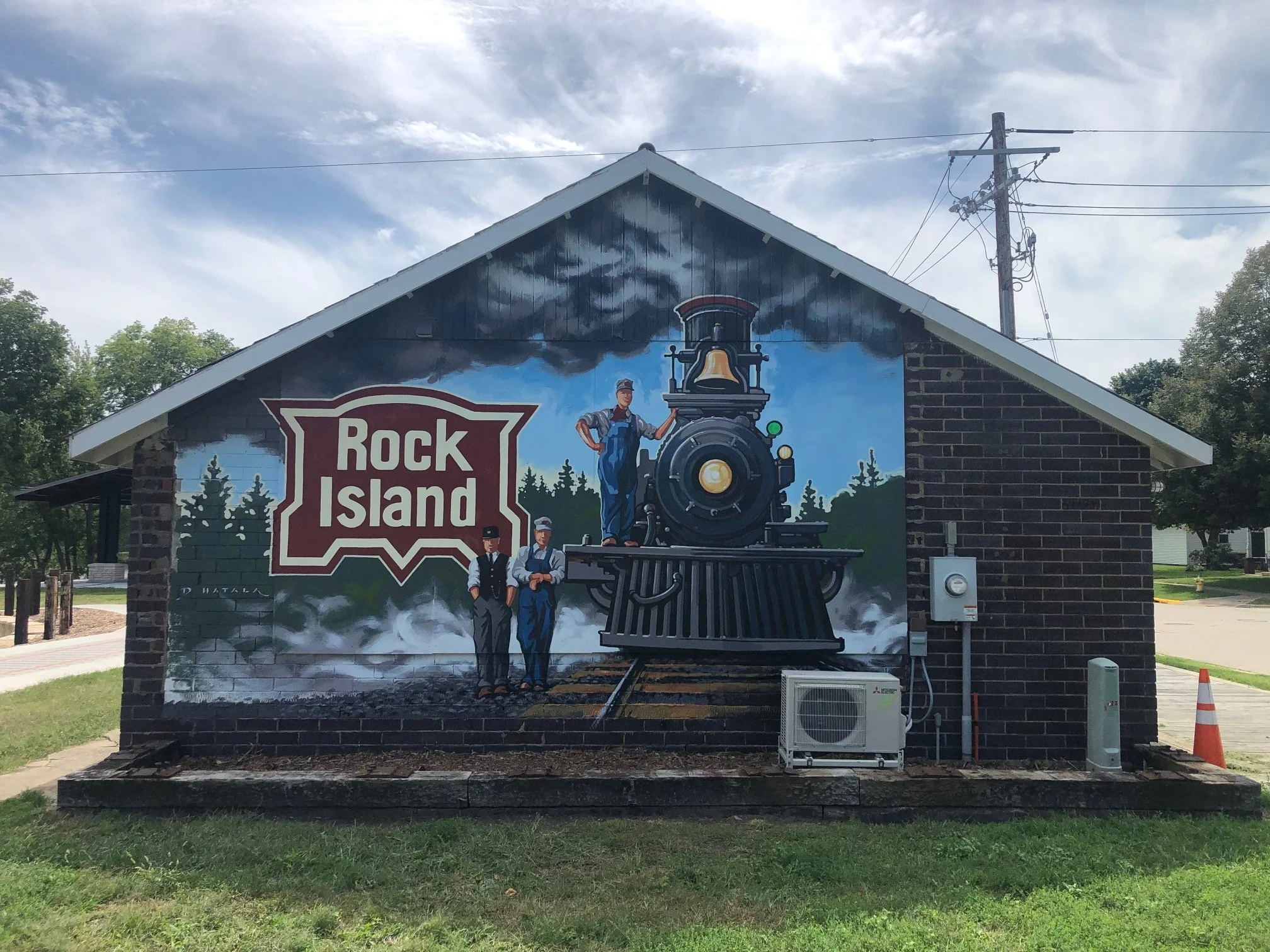Mural on a brick building advertising Rock Island, featuring a vintage steam train with three men standing in front, set against a backdrop of trees and a cloudy sky.