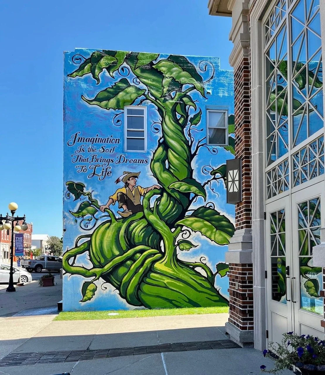 A colorful mural depicting a large twisting green vine with leaves, featuring a person sitting inside it and a quote that reads, "Imagination is the Soil that Brings Dreams to Life."