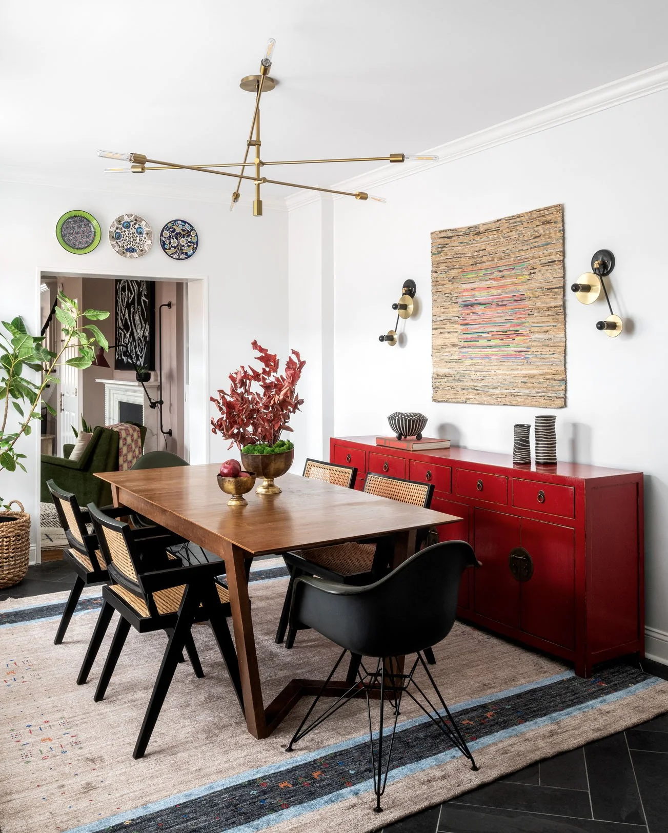 Modern chandelier above wooden dining table with chairs and red credenza