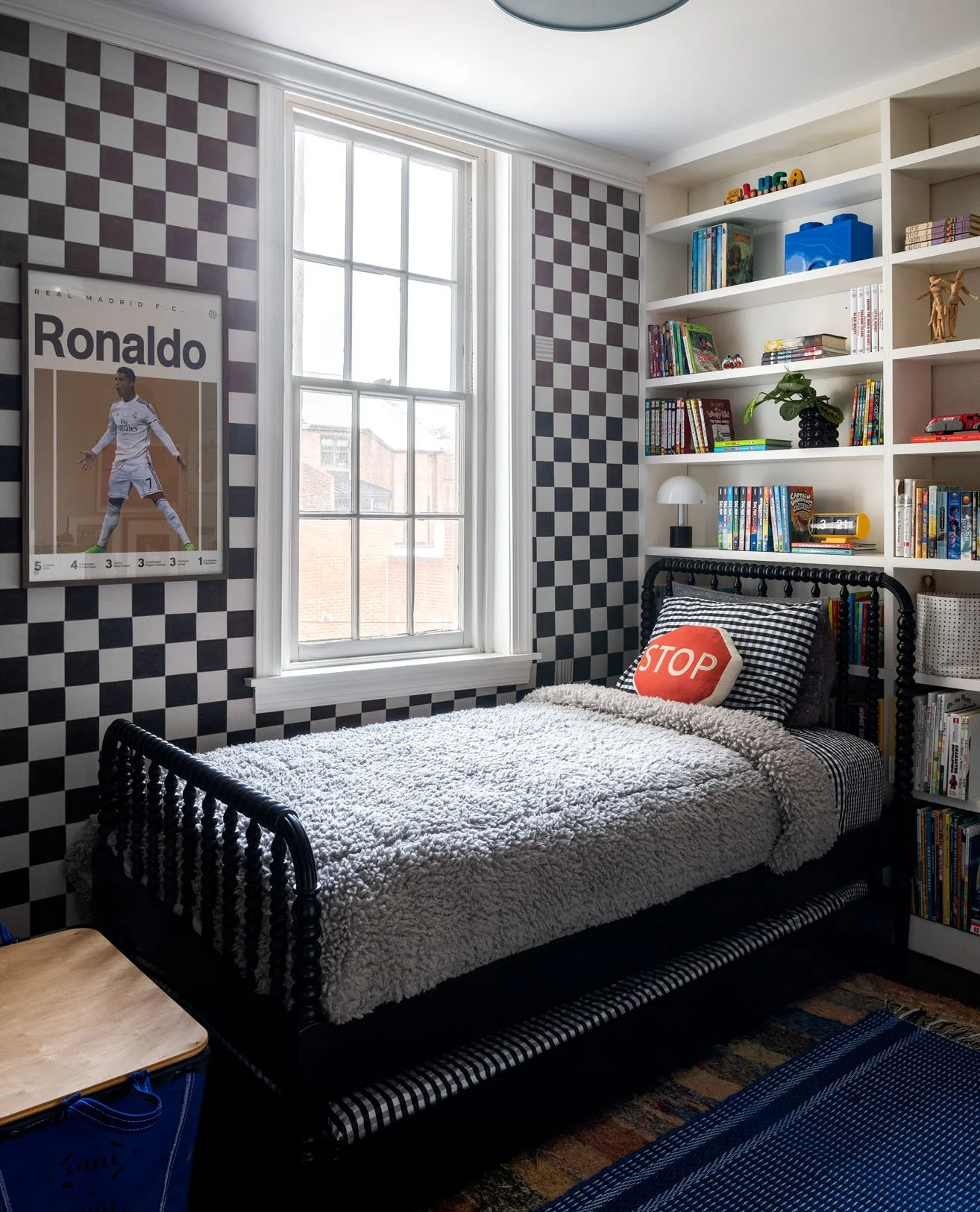 Black twin bed against checkered black and white wallpaper in a child's room