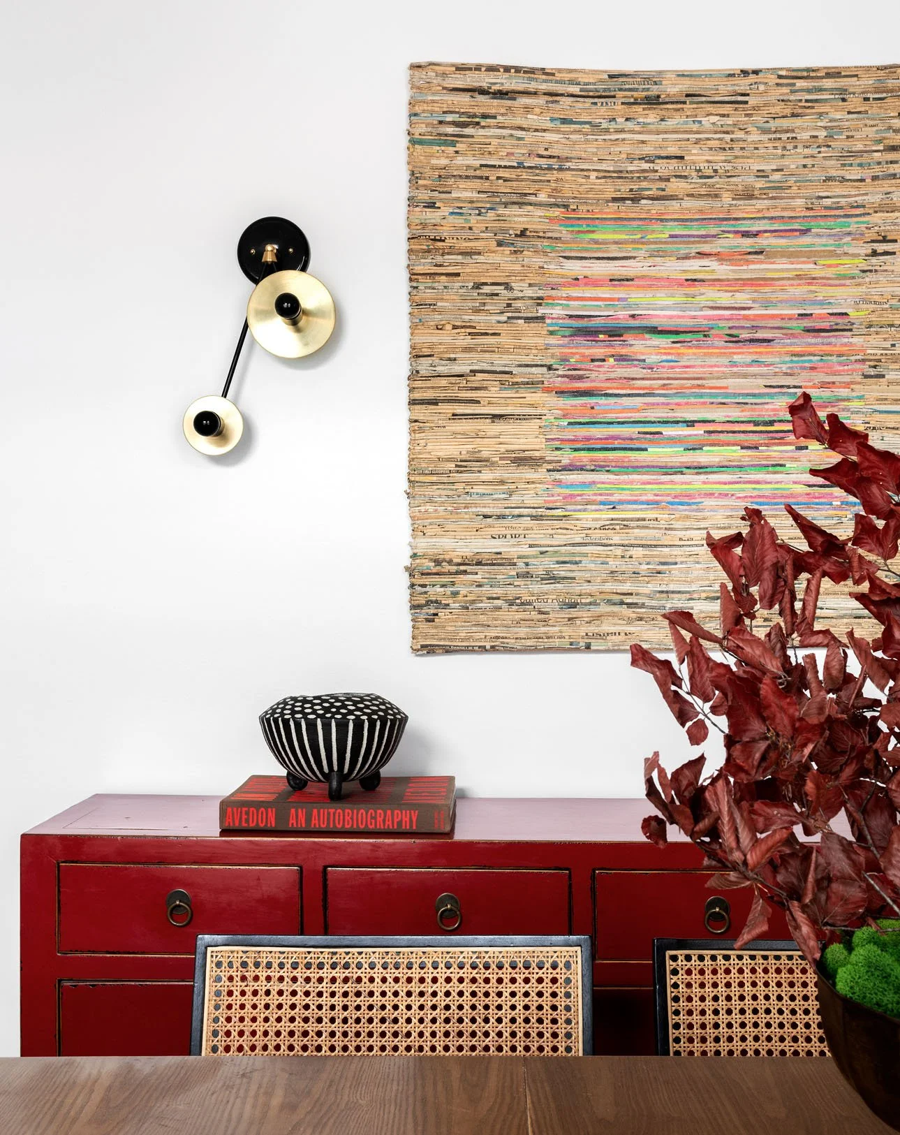 Modern sconce and textured wall hanging above a red credenza