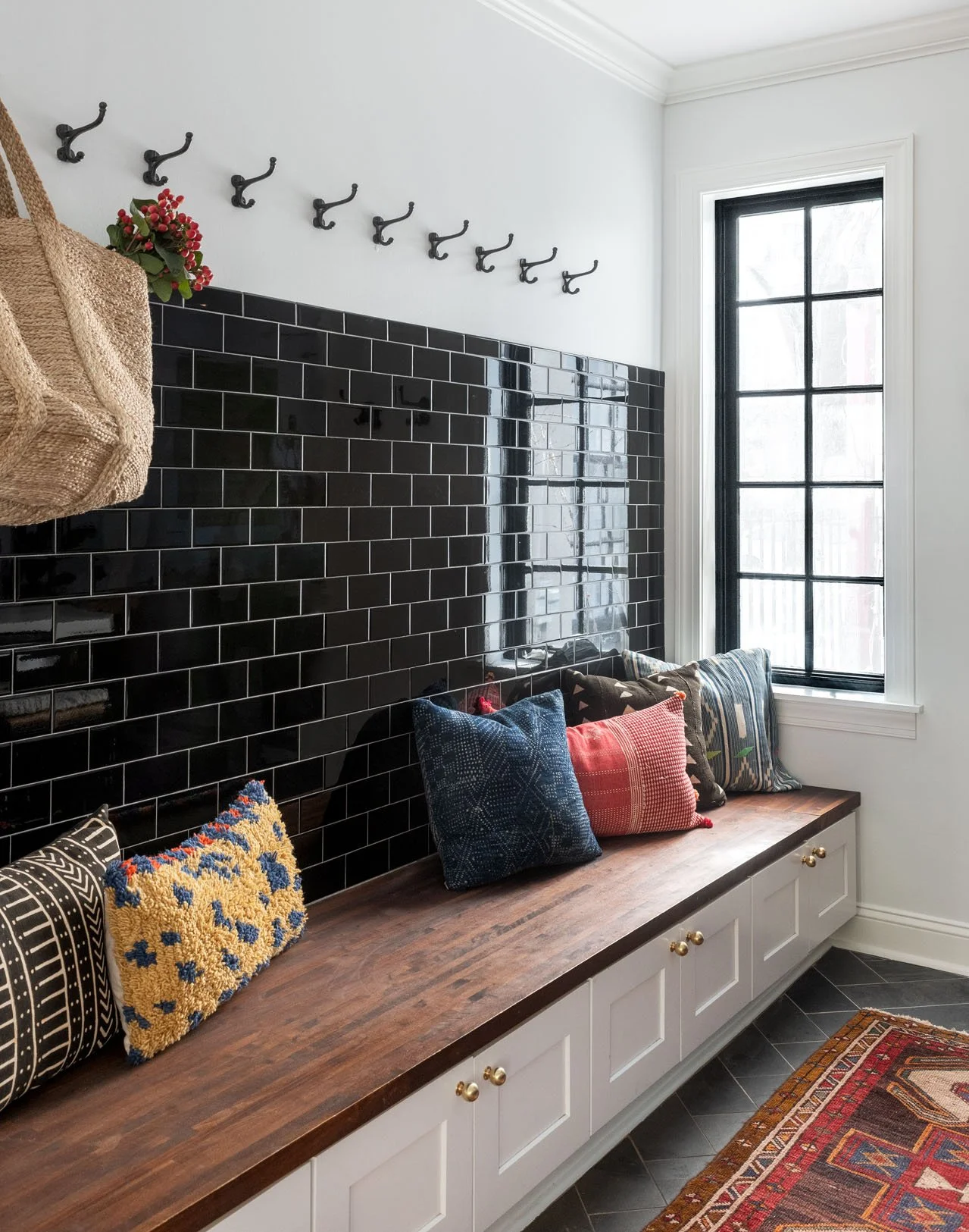 Wooden built in bench against black wall tiles and storage hooks