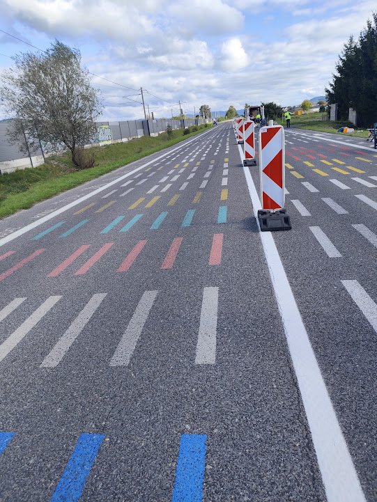 Color-coded bike lane with orange and white barricades along a rural road under a cloudy sky.