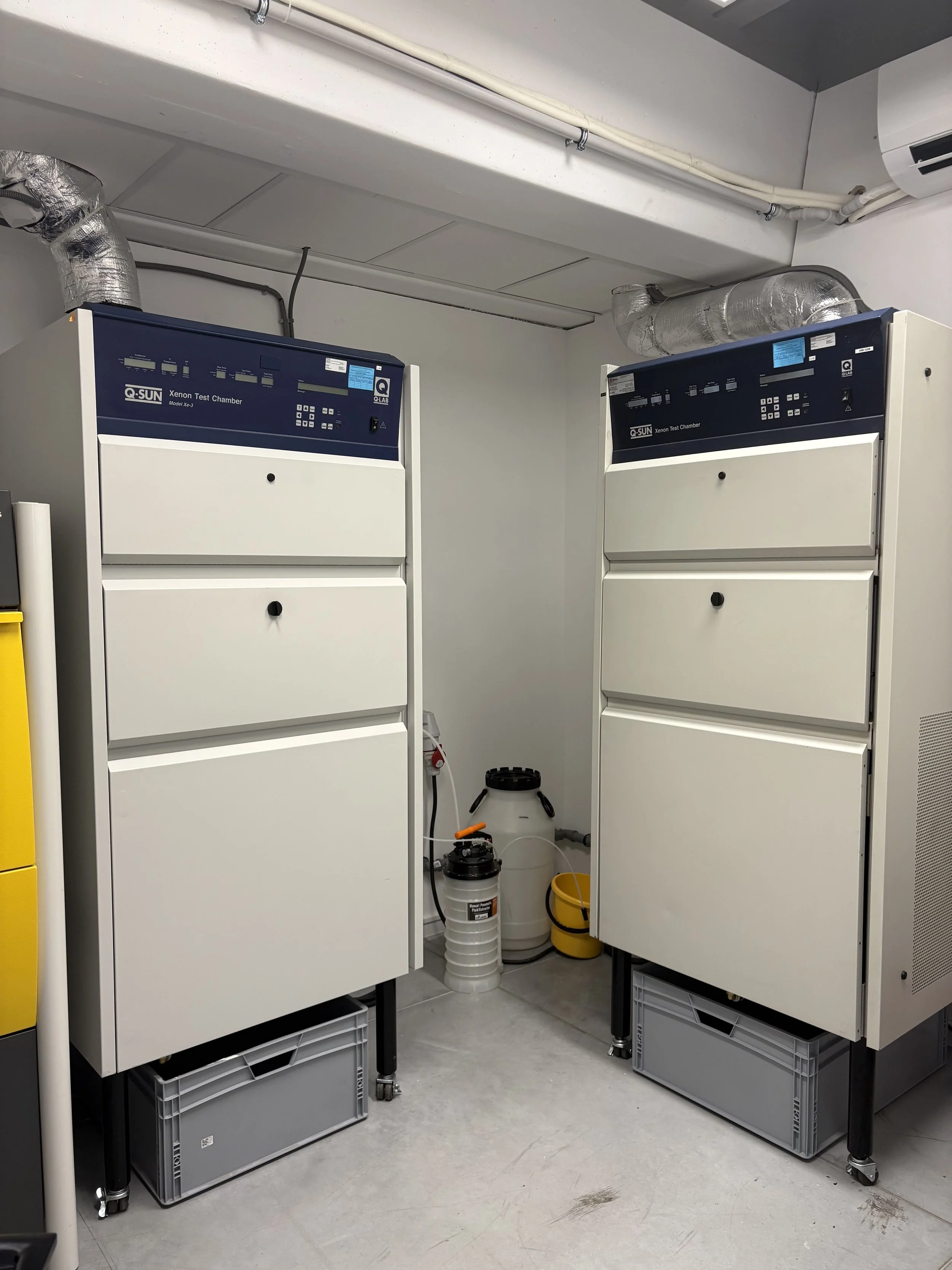 Two xenon test chambers in a laboratory room with ventilation ducts above.