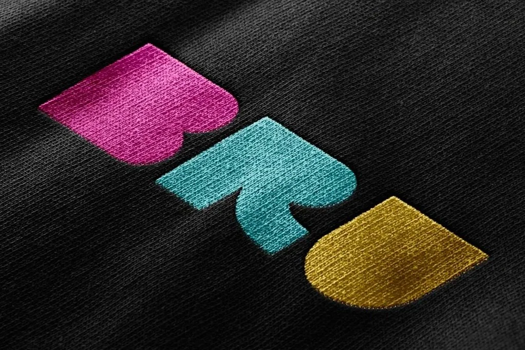 Close-up of a black fabric surface with colorful embroidered shapes in pink, blue, and yellow.