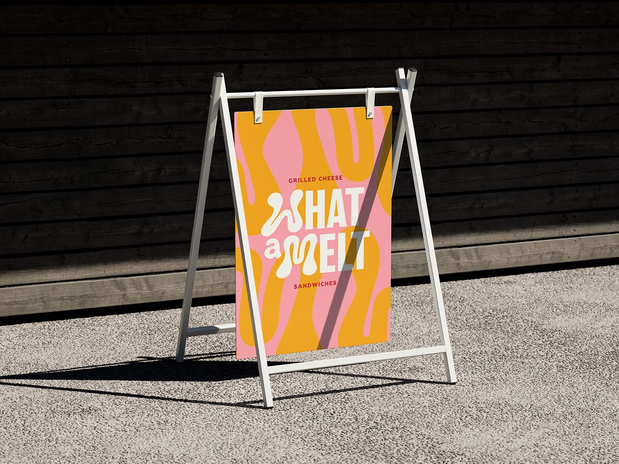 A colorful advertisement sign for a food establishment, featuring pink and orange abstract shapes and the text 'GRILLED CHEESE', 'a SHAT', 'a MELT', and 'SANDWICHES' in white and red lettering, placed on a sidewalk with a wooden background.
