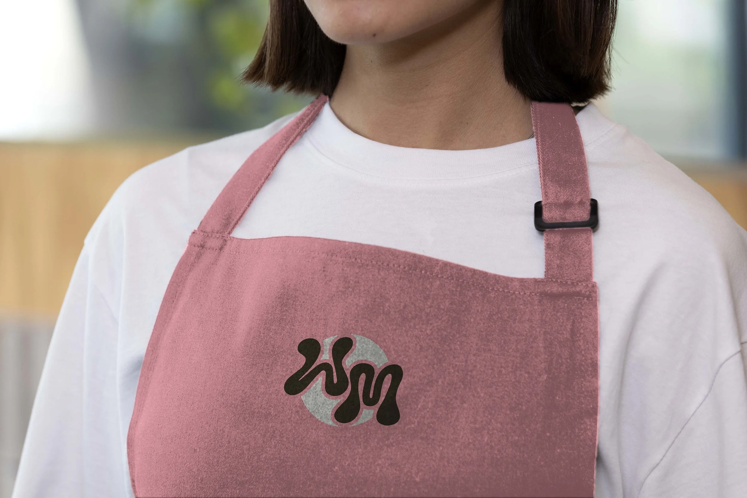 A person wearing a pink apron with a logo on it, over a white t-shirt.