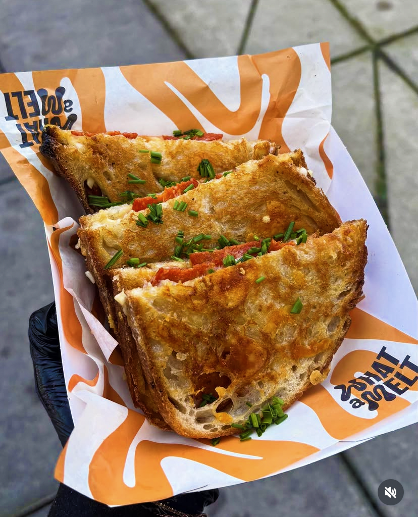 Three slices of French toast topped with chopped chives, served on a paper liner with orange and black branding.