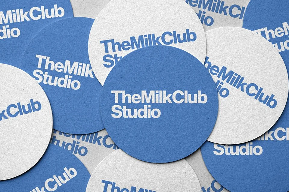 Blue and white circle stickers with 'The Milk Club Studio' text scattered on a surface.
