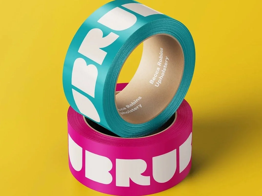 Two rolls of colorful tape, one turquoise with white text and one pink with white text, stacked on a yellow background.